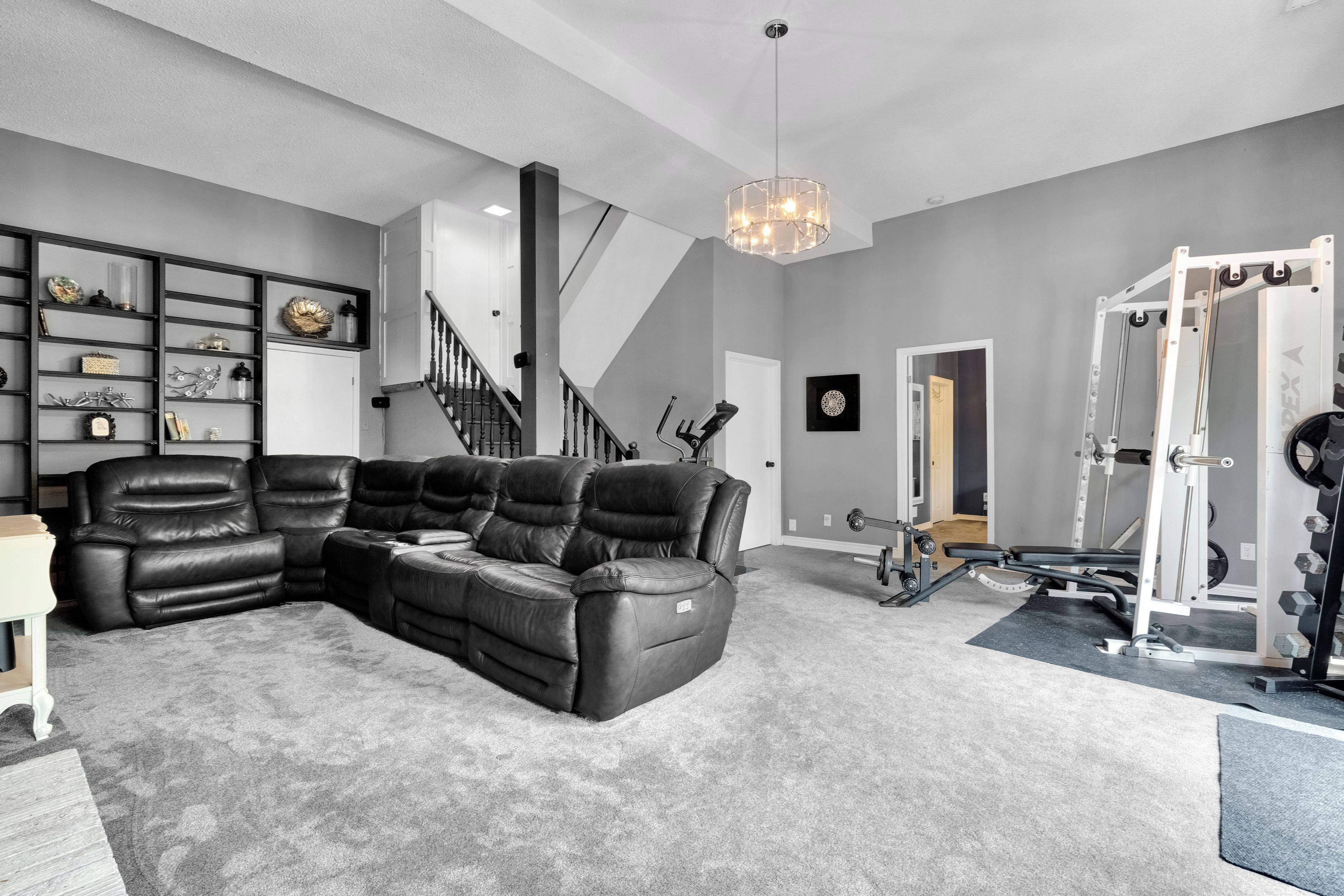 Un salon avec un canapé d’angle, un escalier et une salle de sport.