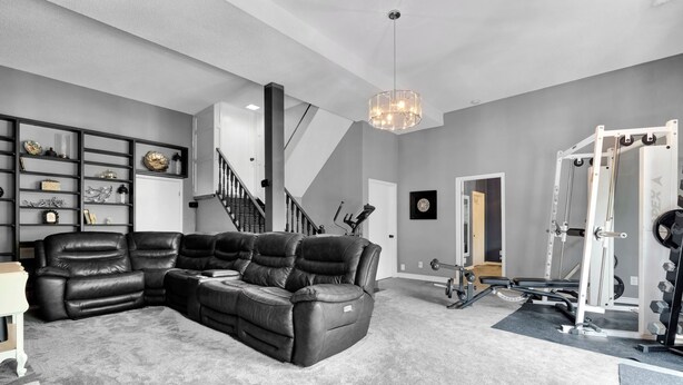 A living room with a sectional sofa, a staircase, and a home gym.