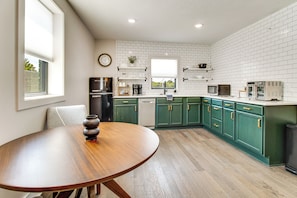 Een moderne keuken met witte metrotegels, groene kasten, een houten eettafel en een inbouwoven.