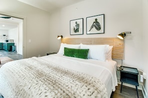 Een hotelkamer met een groot bed, een groen sierkussen en twee kunstwerken in lijsten aan de muur.