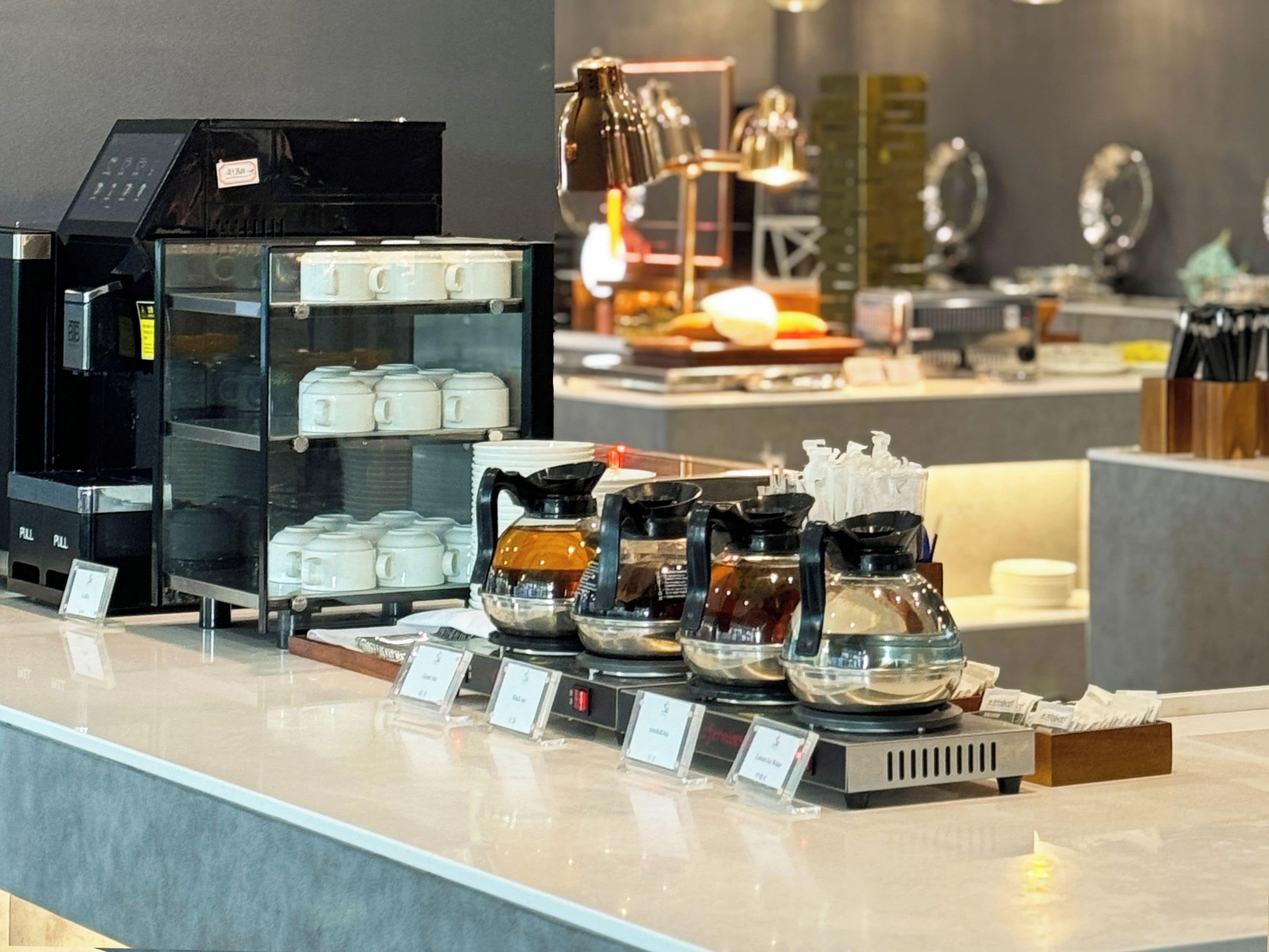 Un coin café équipé d’une machine à café, de théières et d’un présentoir à tasses.