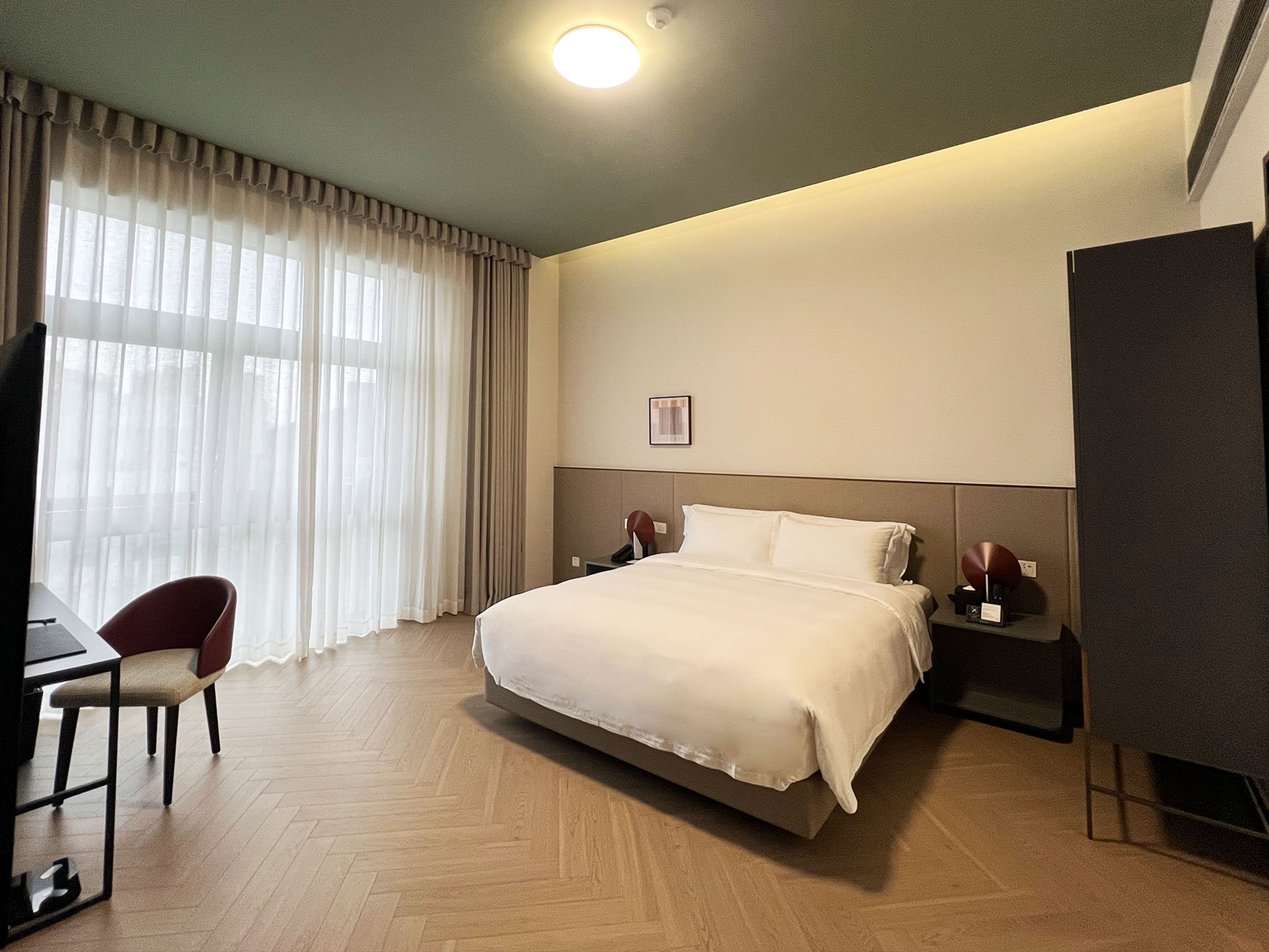 Ein Hotelzimmer mit Bett, Schreibtisch mit Stuhl, Fernseher und Nachttisch mit Lampe.