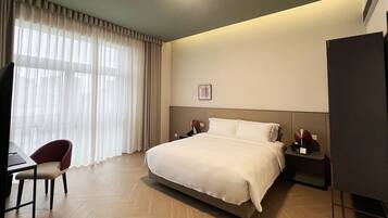 Ein Hotelzimmer mit Bett, Schreibtisch mit Stuhl, Fernseher und Nachttisch mit Lampe.