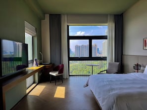 Quarto de hotel com cama, escrivaninha com cadeira, televisão e varanda com vista para edifícios altos.