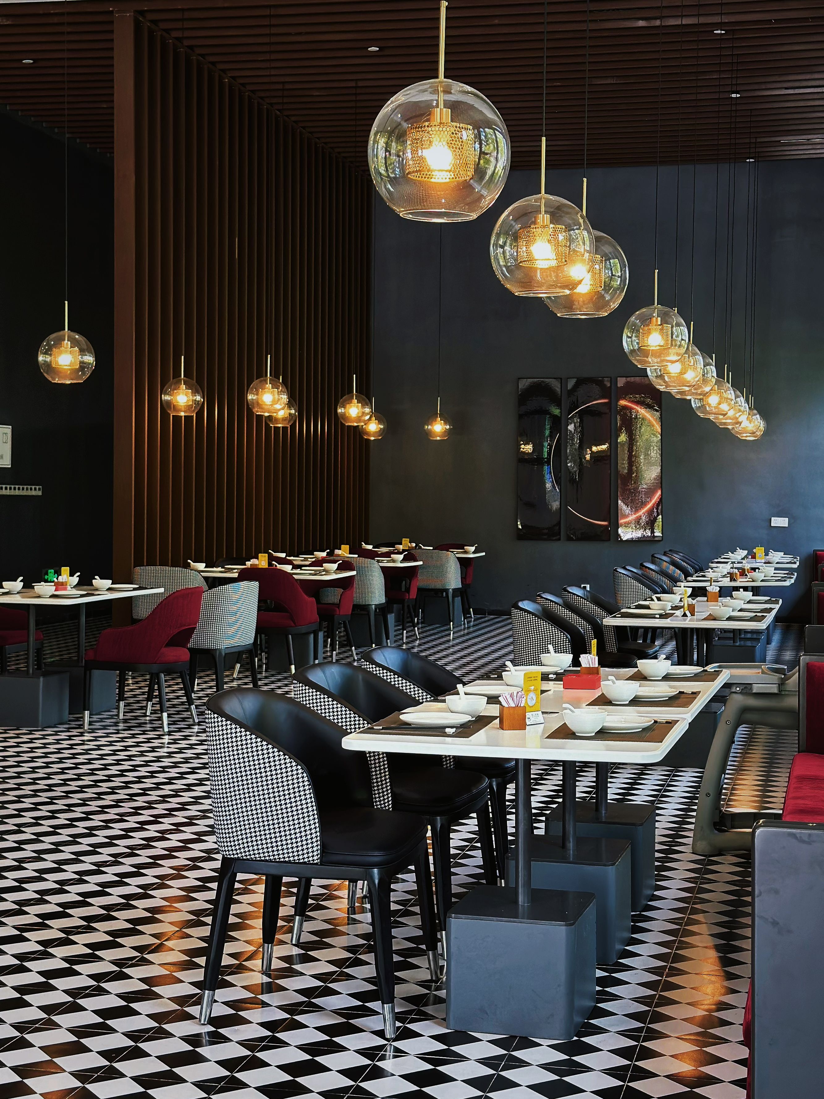 Ein Restaurantinneres mit Schachbrettfußboden, runden Tischen und hängenden, kugelförmigen Leuchten.