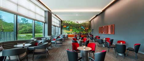 A modern cafe with round tables and chairs, large windows, and a mural on the wall.