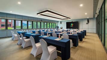 Un salón de conferencias con mesas, sillas y una pantalla grande.