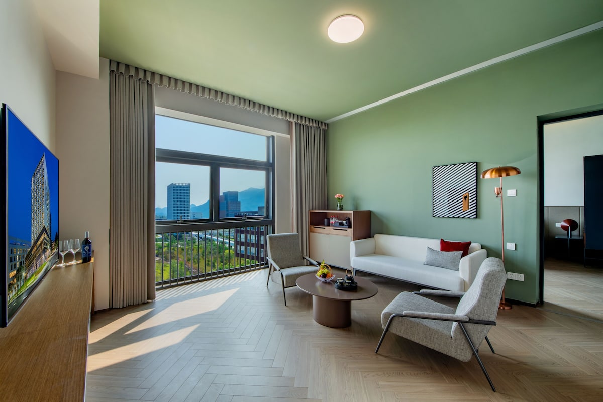 A modern living room with a sofa, chairs, a coffee table, and a view of a cityscape through large windows.