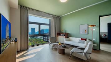 Ein modernes Wohnzimmer mit einer Couch, Sesseln, einem Couchtisch und Blick auf eine Stadtlandschaft durch große Fenster.