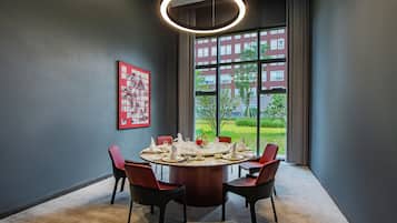 Sala de conferência com mesa redonda, quatro cadeiras e uma janela ampla com vista para edifícios e áreas verdes.