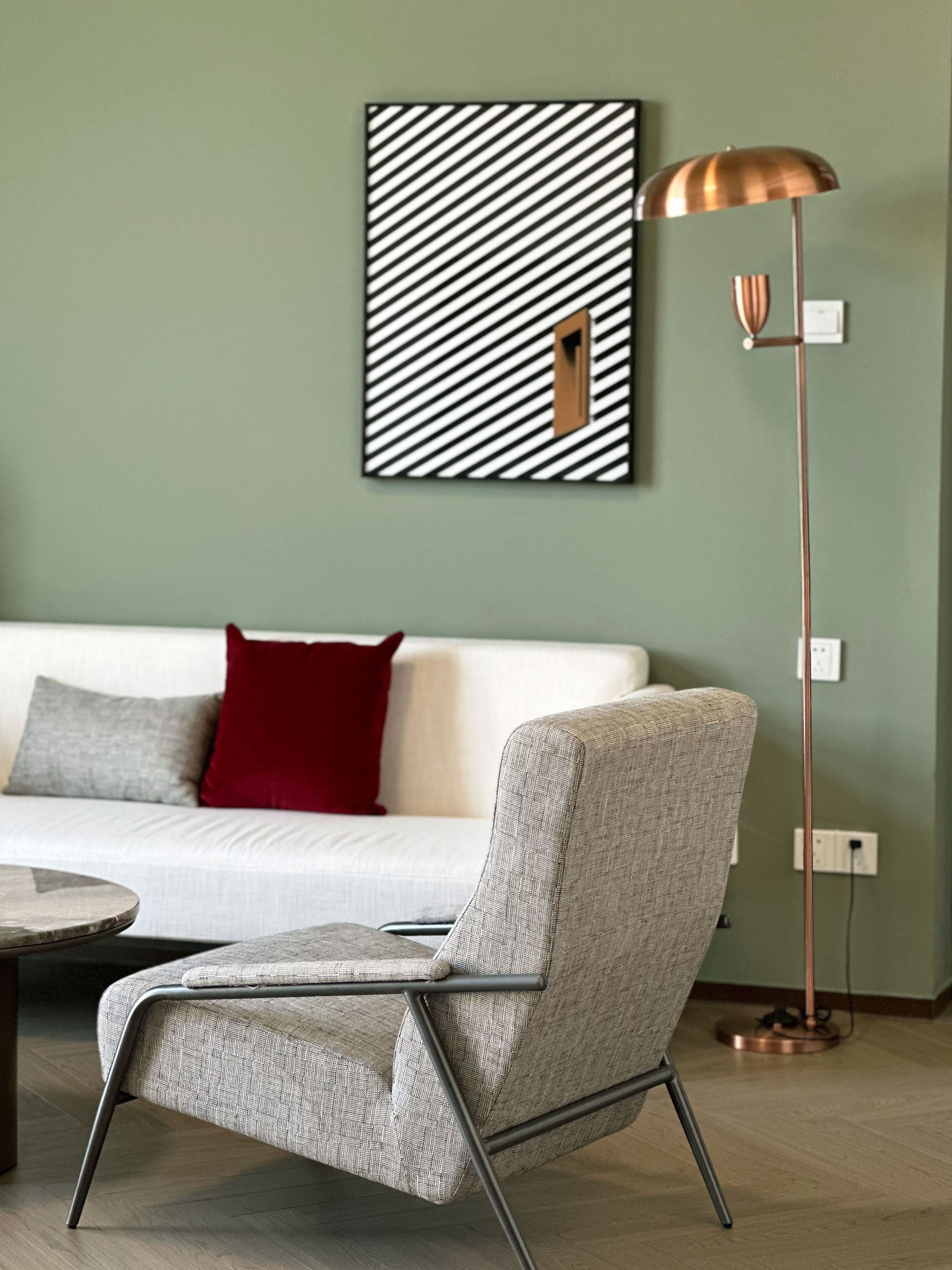 Ein modernes Wohnzimmer mit einer Couch, einem gemusterten Sessel, einer Stehlampe und einem Wandbild.