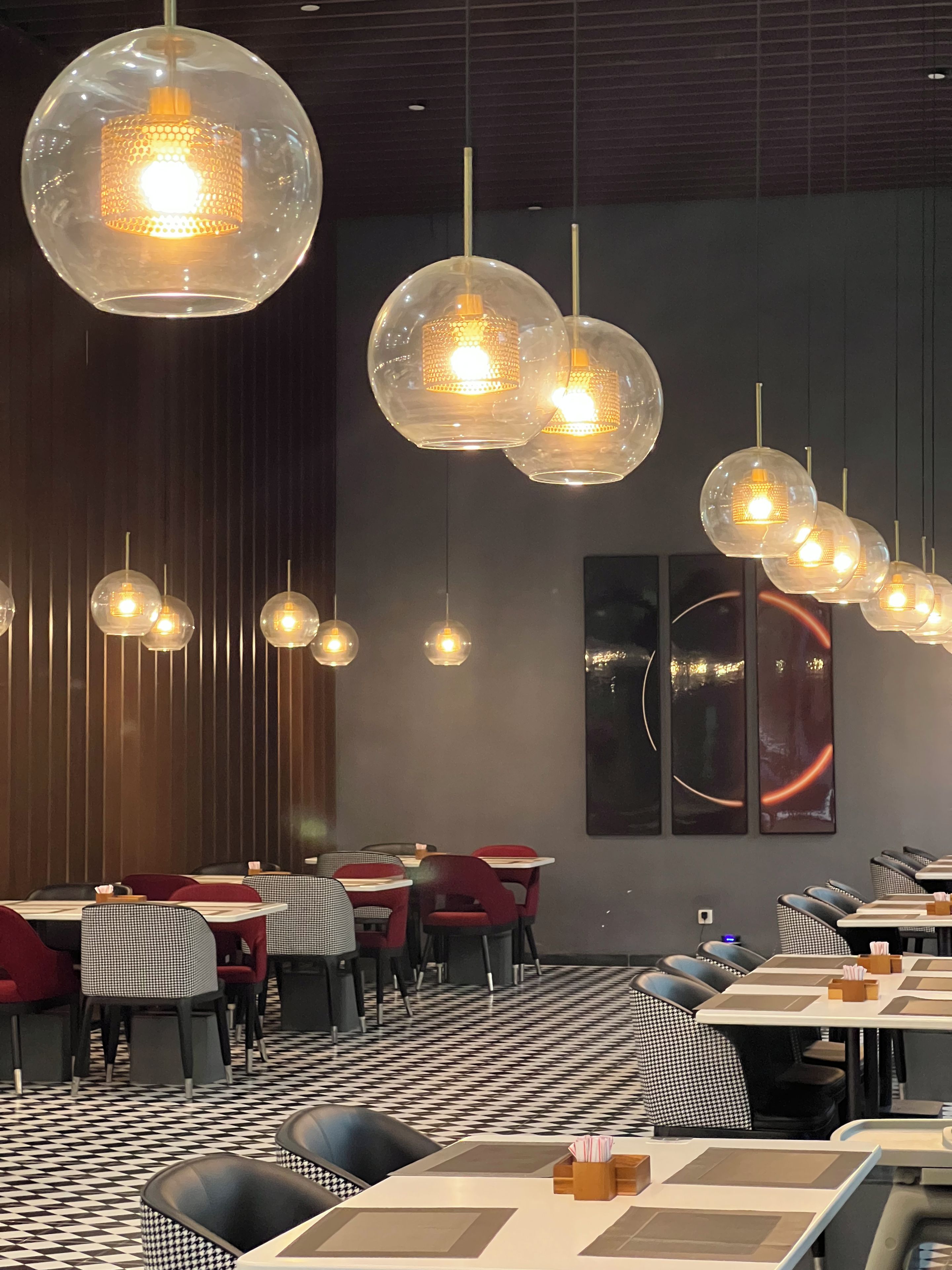 Ein Restaurantinnenraum mit runden, transparenten Pendelleuchten, karierten Tischdecken und einem Schachbrettmuster auf dem Boden.