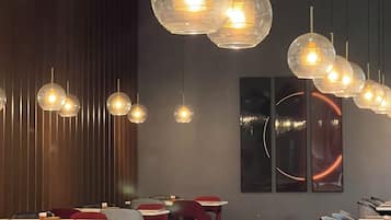 Ein Restaurantinnenraum mit runden, transparenten Pendelleuchten, karierten Tischdecken und einem Schachbrettmuster auf dem Boden.