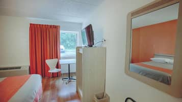 Ein Hotelzimmer mit Bett, Schreibtisch, Stuhl, Fernseher und einem Fenster mit Vorhängen.