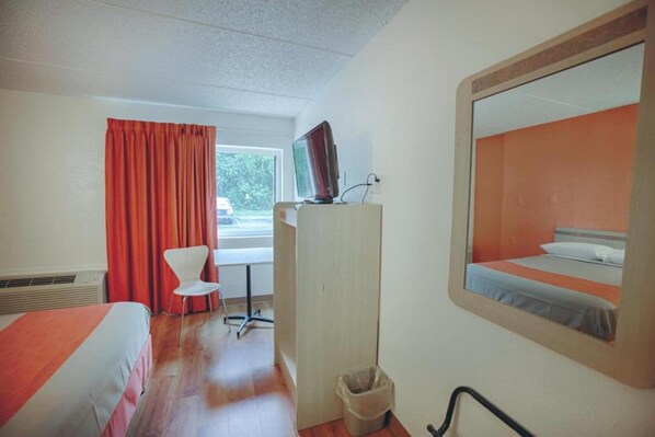 A hotel room with a bed, a desk, a chair, a TV, and a window with curtains.