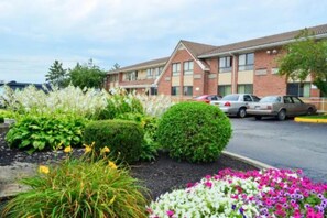 A hotel with a parking lot, a building with a brick facade, and landscaped flower beds.