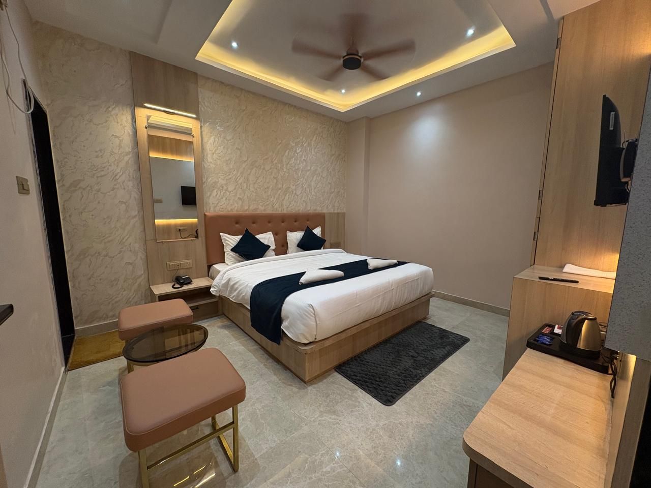 A modern bedroom with a bed, bedside tables, a mirror, a ceiling fan, and a small seating area.