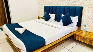 Un letto rifatto con cura, con una testata blu, biancheria bianca e un asciugamano piegato.