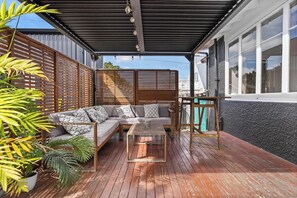 A covered outdoor seating area with a wooden table and a sofa, surrounded by plants. - Spacious 3 Bedroom Villa in Central Whangarei (Whangārei)