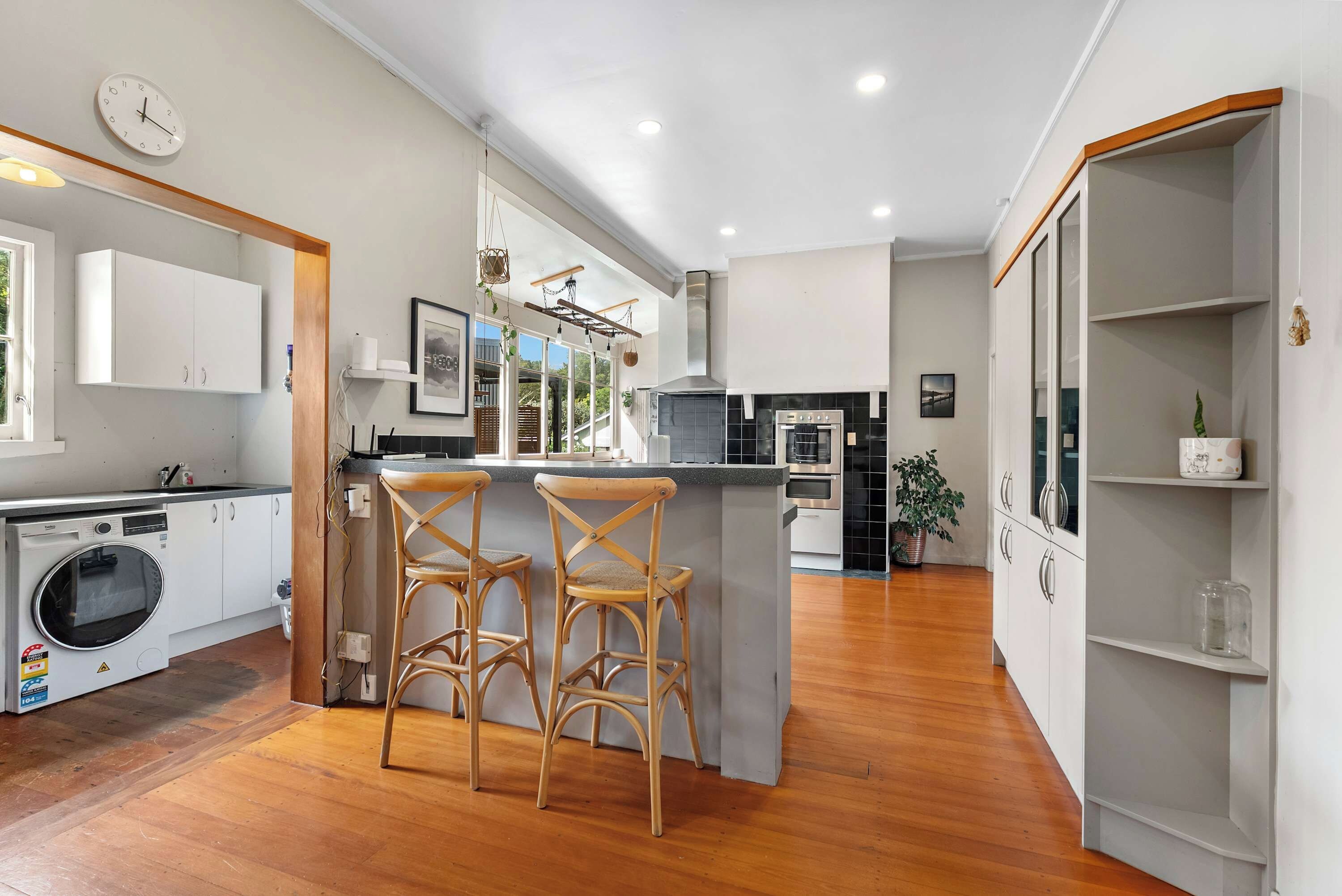 Une cuisine moderne avec un îlot central, des tabourets de bar, un lave-linge et une horloge au mur.