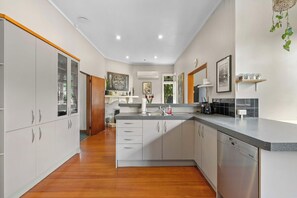 A modern kitchen with white cabinetry, a granite countertop, and a built-in dishwasher. - Spacious 3 Bedroom Villa in Central Whangarei (Whangārei)