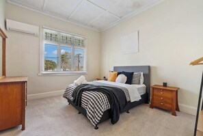 Ein Schlafzimmer mit Bett, Nachttisch, Fenster mit Jalousien und Deckenventilator.