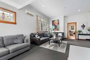 Un salon moderne avec un canapé gris, un divan en cuir noir, une table basse et un tableau accroché au mur.
