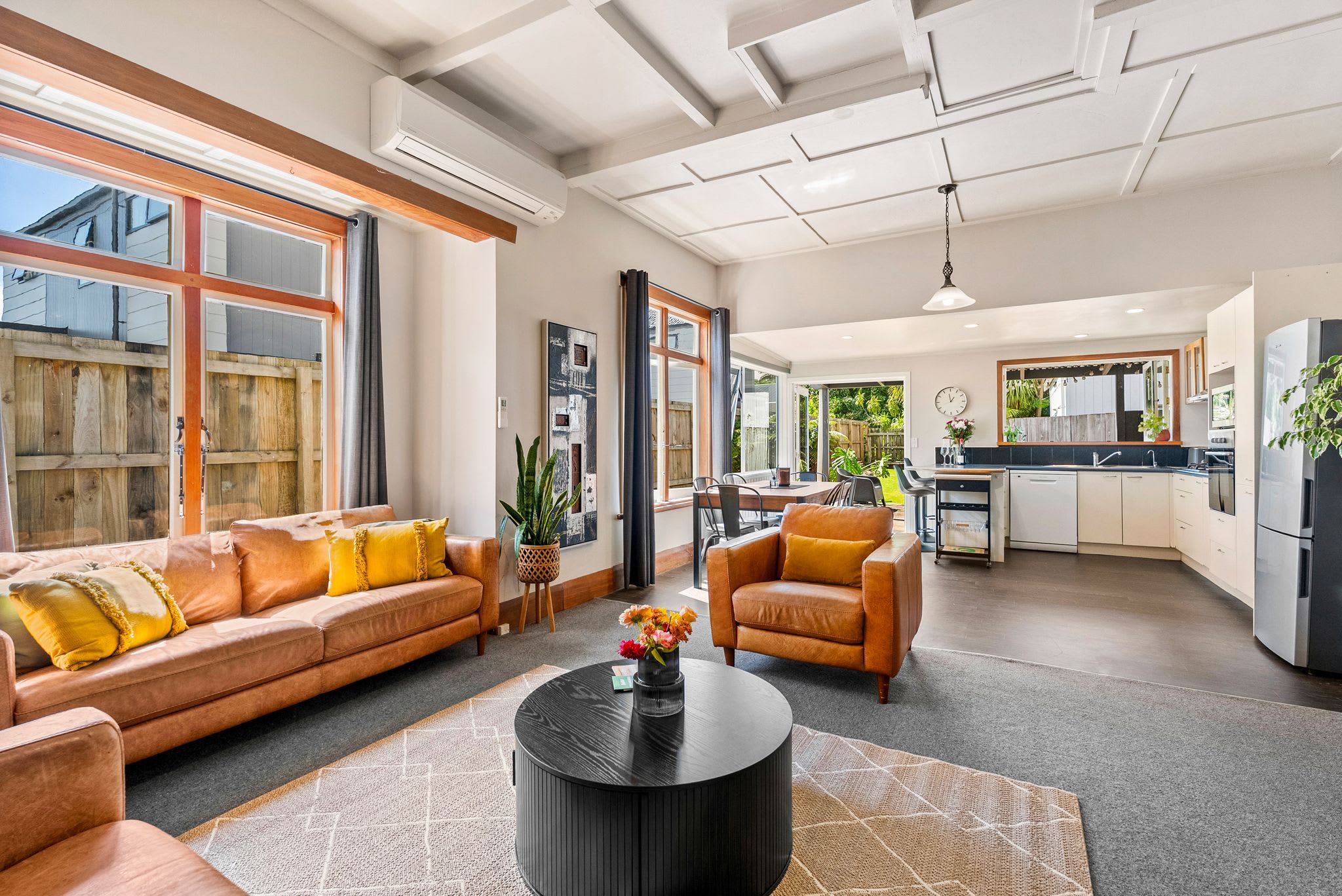 A spacious living area with a sofa, armchair, and coffee table, a kitchen with modern appliances, and a large window providing natural light.