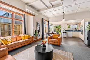 Ein großzügiger Wohnbereich mit Sofa, Sessel und Couchtisch, eine Küche mit modernen Geräten und ein großes Fenster, das für natürliches Licht sorgt.