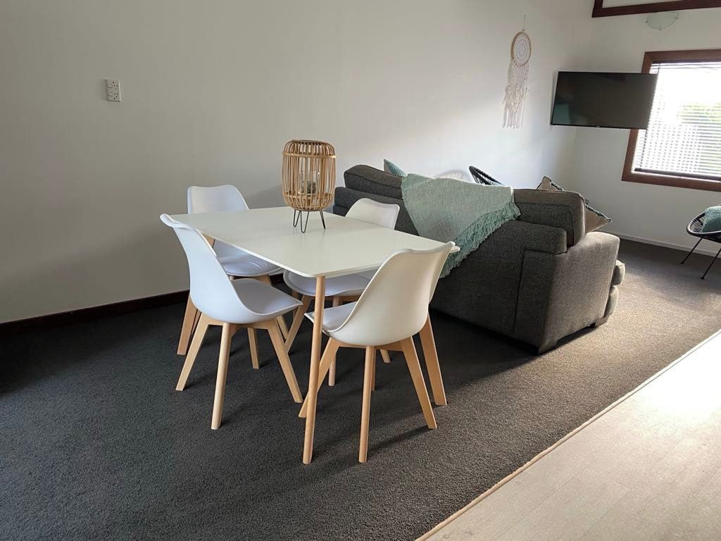 A dining area with a white table and chairs, a grey sofa, and a television mounted on the wall.