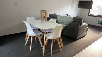 A dining area with a white table and chairs, a grey sofa, and a television mounted on the wall.