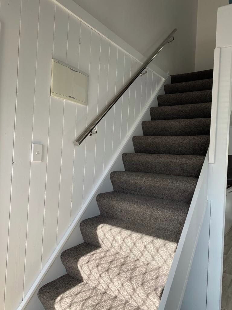 Un escalier avec des marches recouvertes de moquette et une rampe métallique.