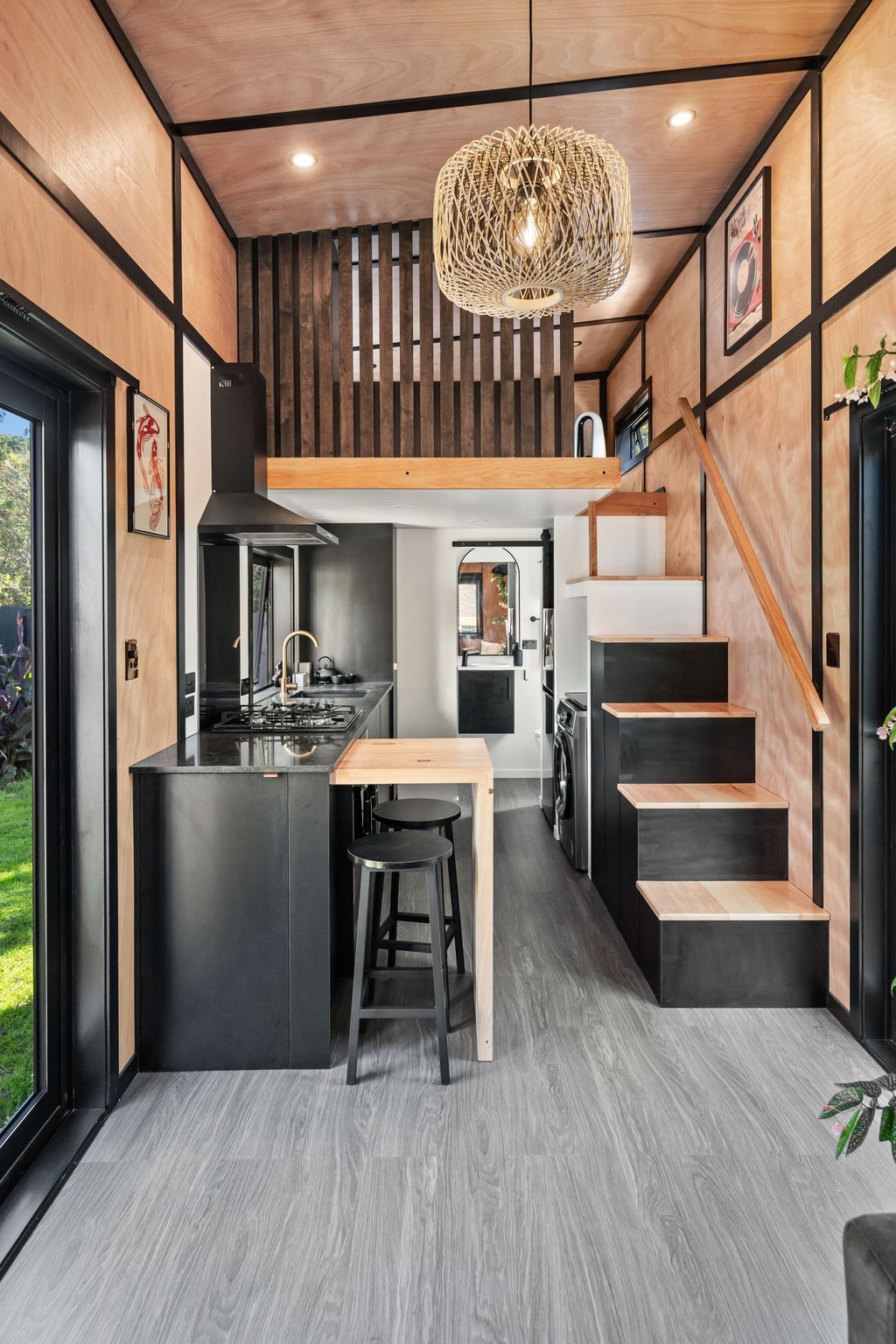 A modern kitchen with a central island, wooden staircase, and a hanging light fixture.