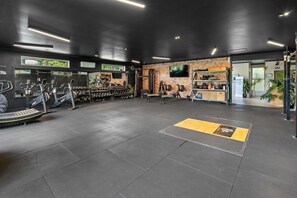 Une salle de sport équipée de matériel d’exercice, avec un mur en briques et un téléviseur.