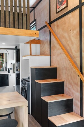 Une cuisine moderne équipée d’un lave-linge intégré, d’une table à manger en bois et d’un escalier avec des marches noires.
