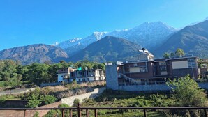 A residential area with modern buildings, a stone wall, and a mountain range in the background. - Mountain Monk (Kalpa)