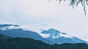 A mountainous landscape with dense forested hills and a mountain peak partially obscured by clouds. - Mountain Monk (Kalpa)