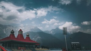 A stadium with a red-roofed building, a scoreboard, and mountains in the background. - Mountain Monk (Kalpa)