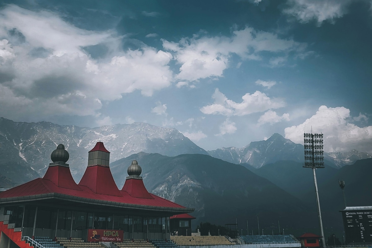 Uno stadio con un edificio a tetto rosso, un tabellone dei punteggi e montagne sullo sfondo.