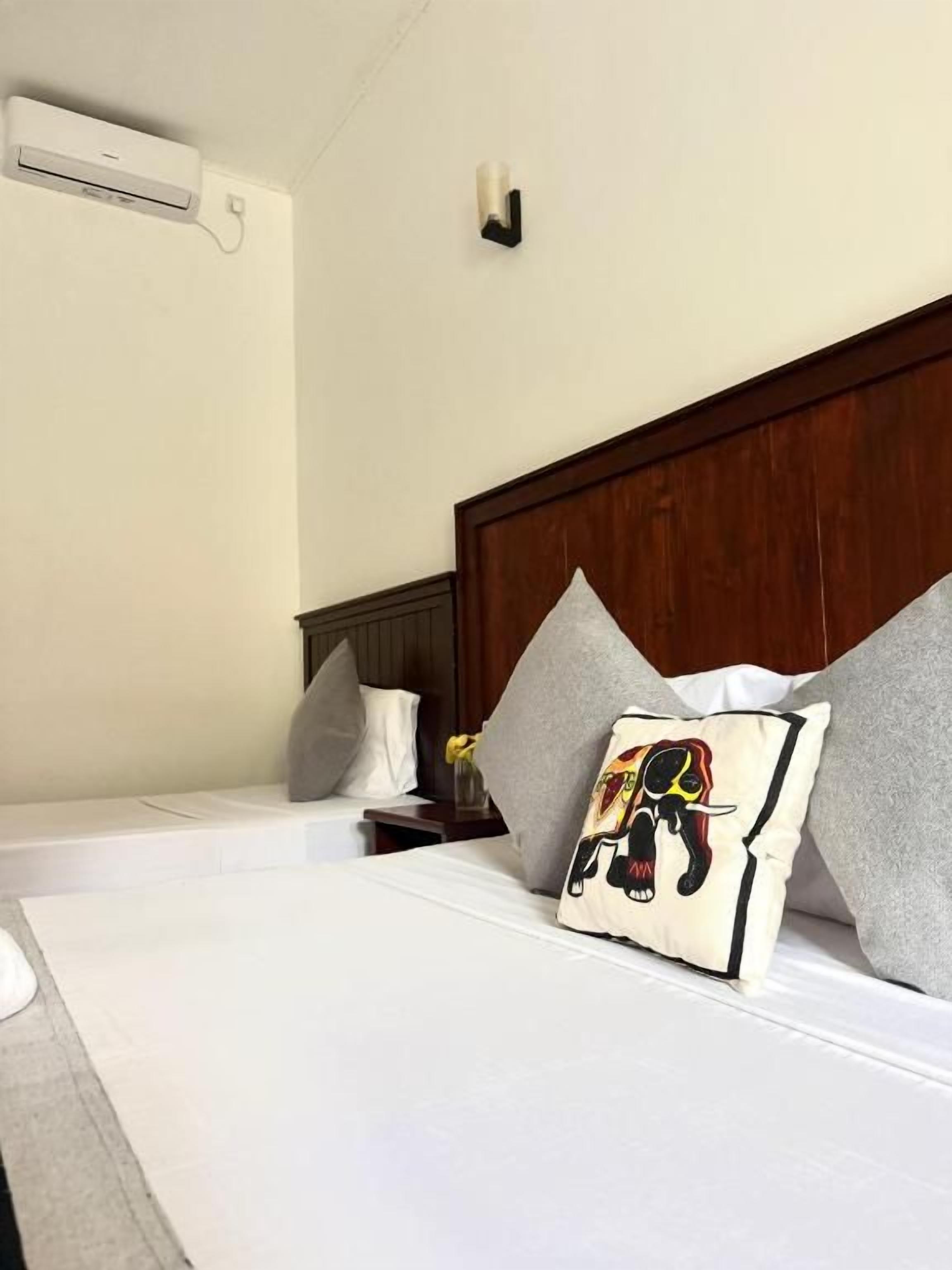 Una camera d'albergo con un letto, cuscini, un comodino e un condizionatore d'aria a parete.