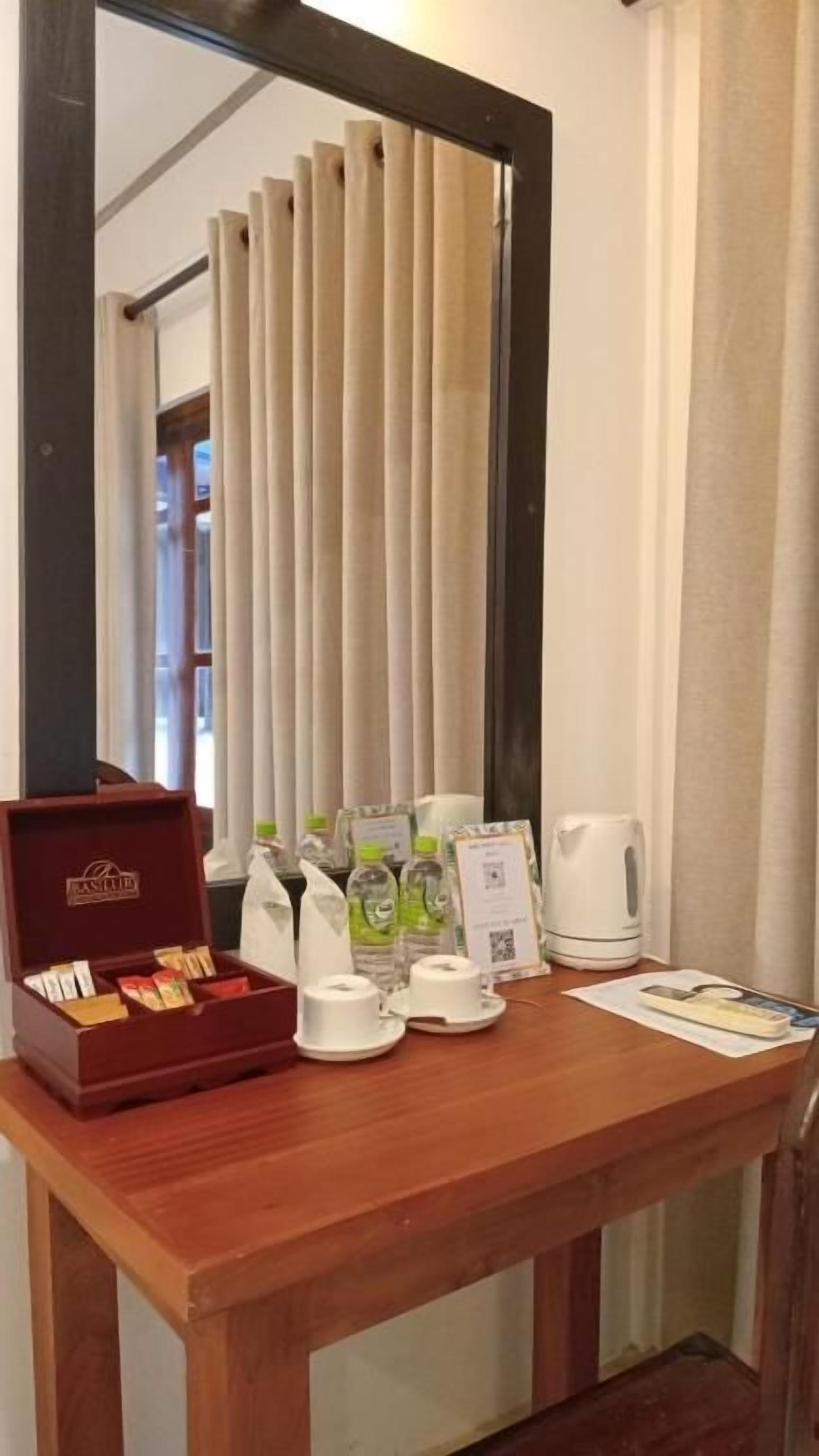 A wooden table with a coffee maker, cups, a box of chocolates, and a menu.
