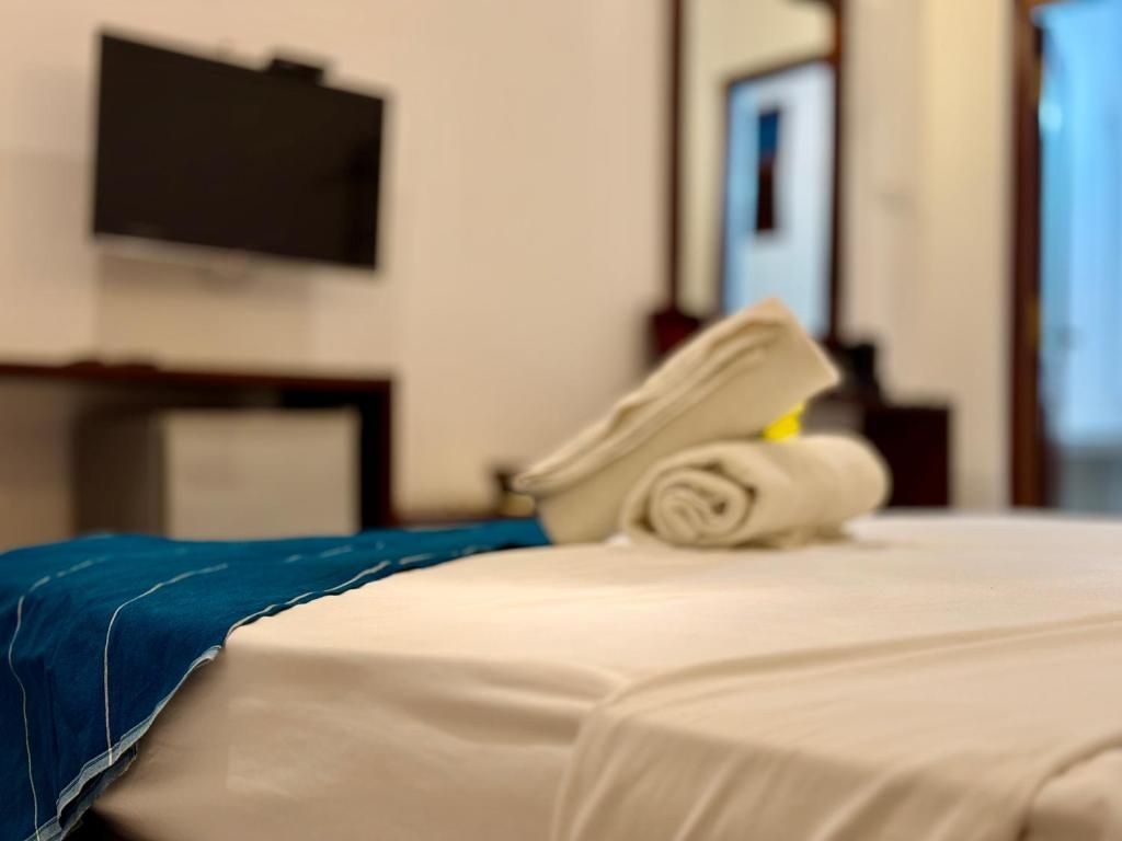A hotel room with a bed, a folded towel, and a flat-screen TV mounted on the wall.