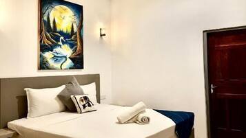A bedroom with a bed, a ceiling fan, a painting, and a door.