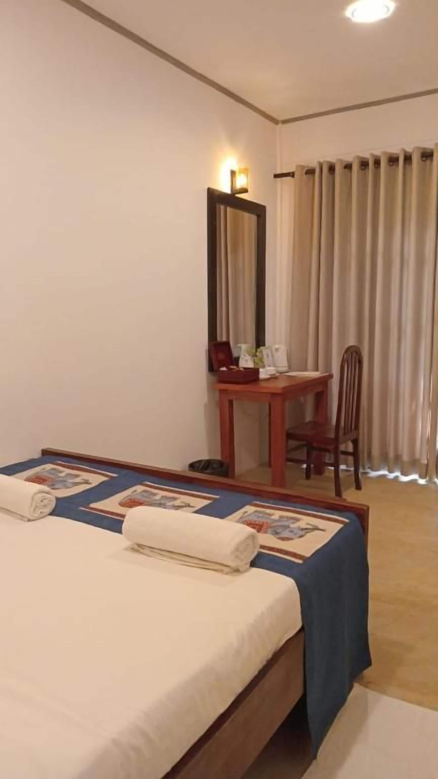 A hotel room with a bed, a desk, a chair, a mirror, and a window with curtains.