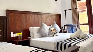 A hotel room with a wooden headboard, two beds with striped bedding, a nightstand with a vase of flowers, and a window with a view of the outside. - Hiri point villa (Dikwella)