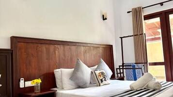 Una habitación de hotel con cabecera de madera, cama con ropa de cama a rayas, mesita de noche con un florero y una ventana con cortinas.