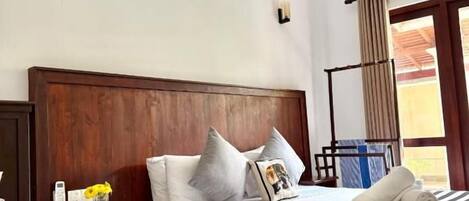 Una habitación de hotel con cabecera de madera, cama con ropa de cama a rayas, mesita de noche con un florero y una ventana con cortinas.