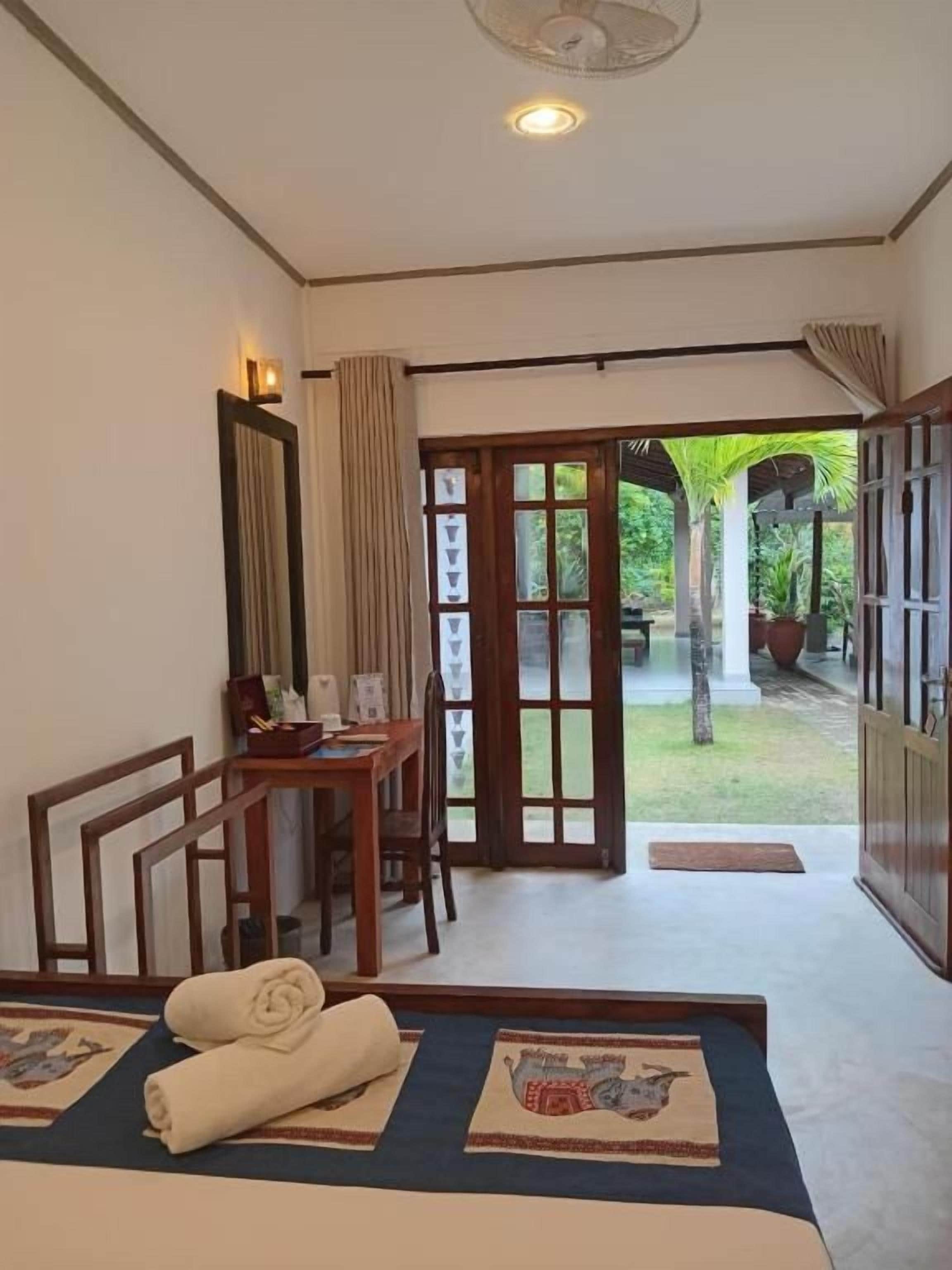 A hotel room with a bed, a desk, and a view of the garden through the door.