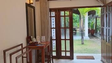 A hotel room with a bed, a desk, and a view of the garden through the door.