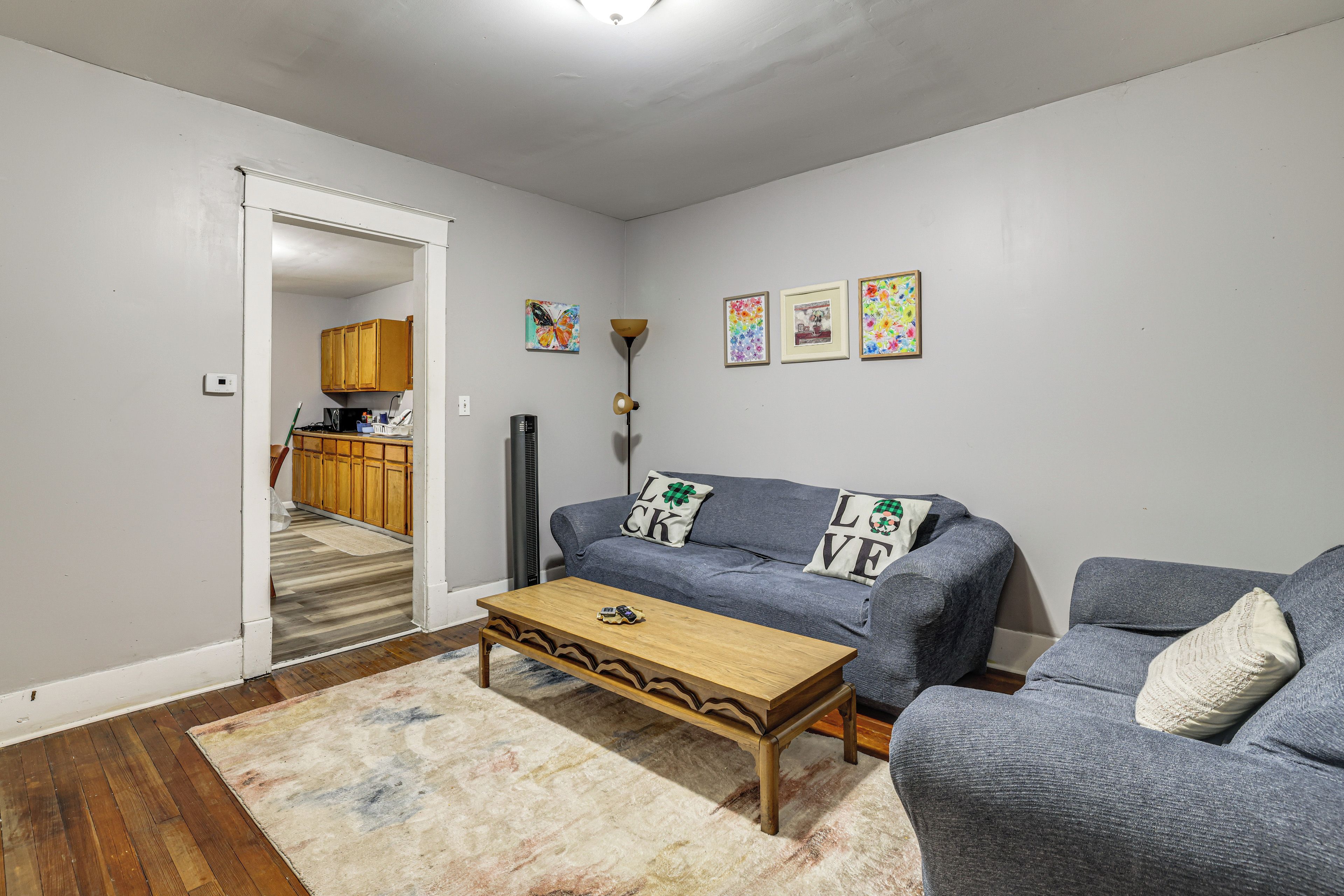 A living room with a sofa, a coffee table, and a rug. There is a kitchen in the background.